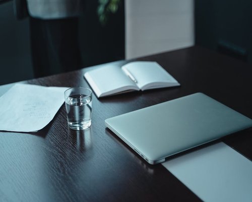 Glass of water resting on a wooden office desk next to a notebook